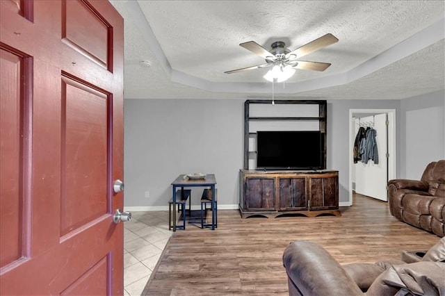 living room with a textured ceiling, ceiling fan, and a tray ceiling