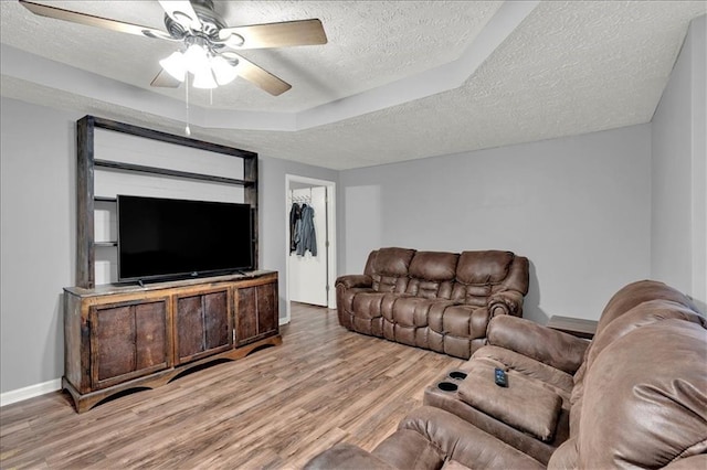 living room featuring ceiling fan, a textured ceiling, a tray ceiling, and light wood-type flooring