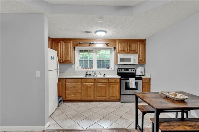 kitchen featuring a textured ceiling, light tile patterned floors, sink, and white appliances