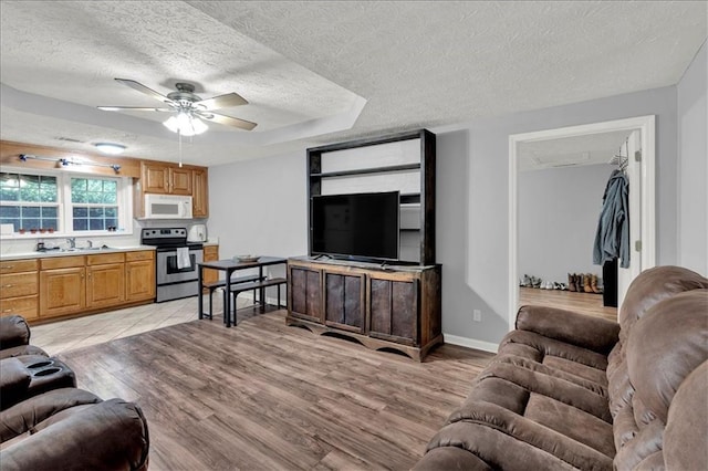 living room with ceiling fan, a raised ceiling, a textured ceiling, light hardwood / wood-style flooring, and sink