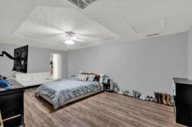 bedroom featuring ceiling fan, wood-type flooring, a tray ceiling, and a textured ceiling