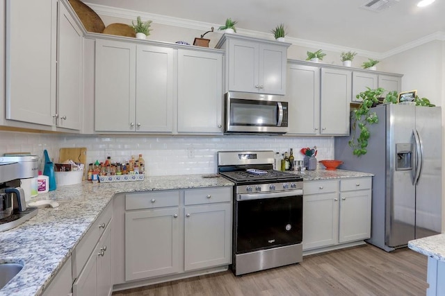 6721 Moondancer Ct, Flowery Branch, GA 30542 - kitchen with stainless steel appliances, light wood-style flooring, decorative backsplash, ornamental molding, and light stone counters