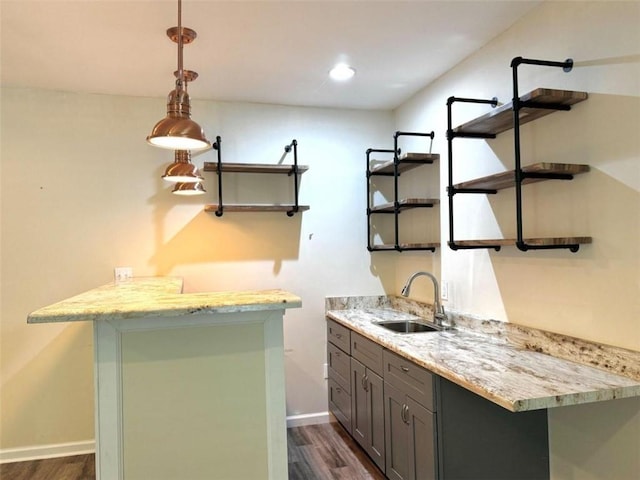 bar with dark hardwood / wood-style flooring, light stone countertops, sink, and pendant lighting