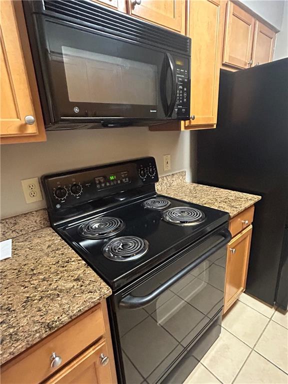 kitchen with light tile patterned flooring, light stone counters, and black appliances