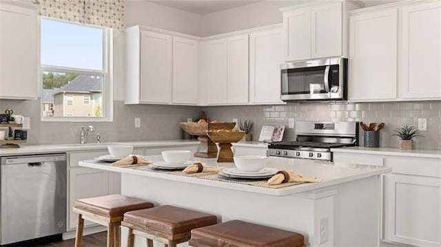 kitchen featuring appliances with stainless steel finishes, white cabinetry, backsplash, and a breakfast bar area