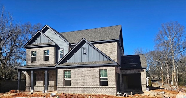 view of front facade featuring covered porch, brick siding, and board and batten siding