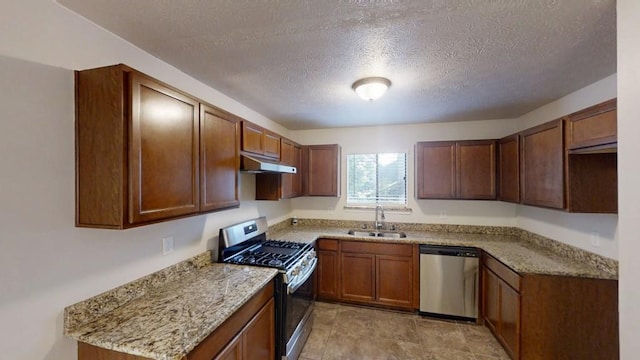 1169 Oaks Pl, Stone Mountain, GA 30083 - kitchen featuring stainless steel appliances, under cabinet range hood, a textured ceiling, light stone counters, and brown cabinetry