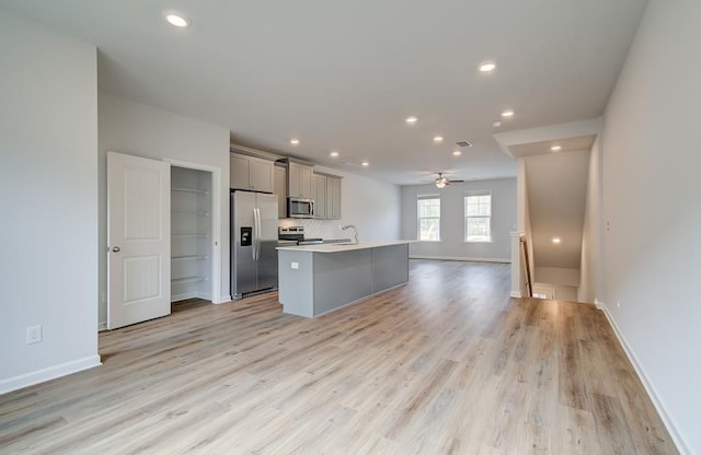 kitchen featuring open floor plan, light countertops, appliances with stainless steel finishes, gray cabinets, and a center island with sink