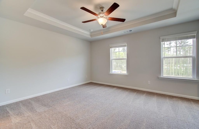 carpeted empty room featuring a raised ceiling, visible vents, ornamental molding, a ceiling fan, and baseboards