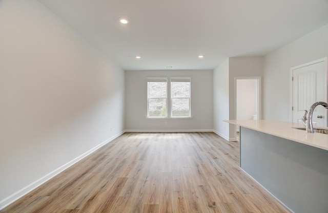 unfurnished living room with light wood-type flooring, baseboards, a sink, and recessed lighting