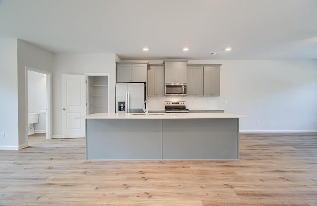 kitchen with appliances with stainless steel finishes, light countertops, gray cabinets, and a kitchen island with sink