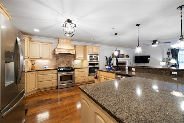 kitchen featuring decorative backsplash, appliances with stainless steel finishes, wood finished floors, cream cabinets, and custom exhaust hood