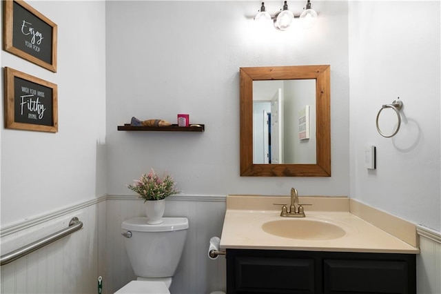 half bath featuring toilet, vanity, and wainscoting