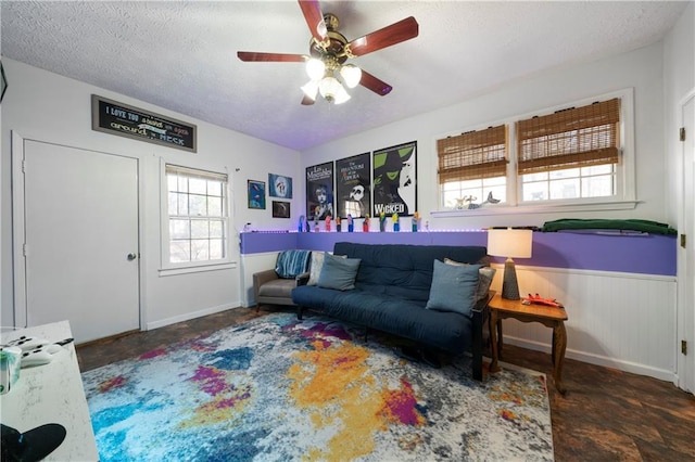 living area featuring a ceiling fan, wainscoting, and a textured ceiling