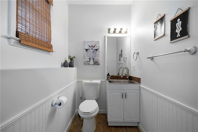 half bathroom with wainscoting, vanity, and toilet