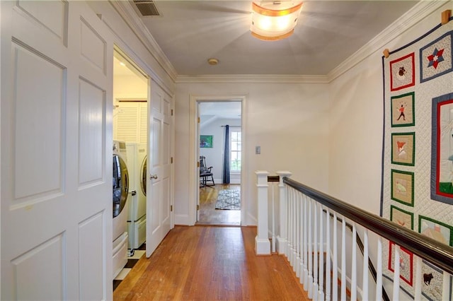 corridor with baseboards, an upstairs landing, light wood-type flooring, visible vents, and ornamental molding