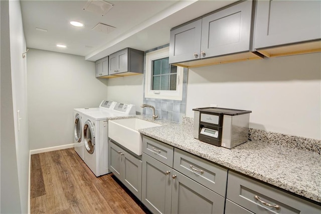laundry room featuring cabinet space, a sink, baseboards, wood finished floors, and washing machine and dryer