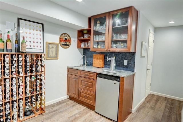 bar featuring tasteful backsplash, fridge, a sink, indoor wet bar, and light wood finished floors