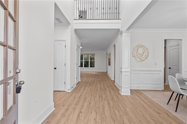 foyer featuring light wood-style floors, decorative columns, a decorative wall, and crown molding