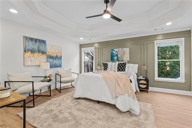 bedroom with wood finished floors, a raised ceiling, visible vents, and crown molding