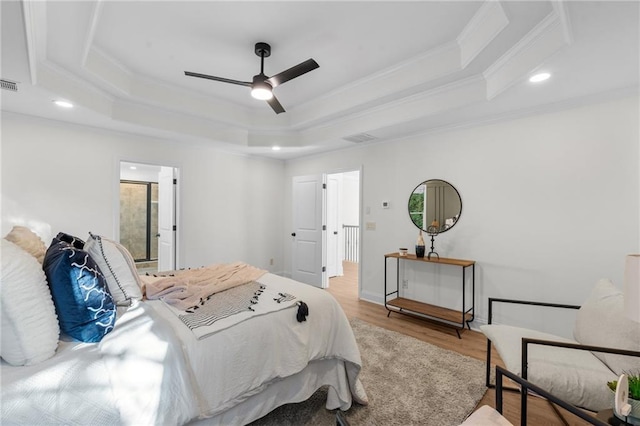 bedroom featuring light wood-style flooring, visible vents, a tray ceiling, and ornamental molding