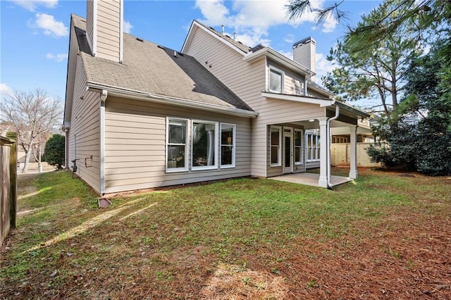 rear view of property with a patio, roof with shingles, a chimney, and a lawn