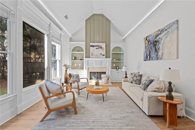 living room with built in features, lofted ceiling, a fireplace, and light wood finished floors