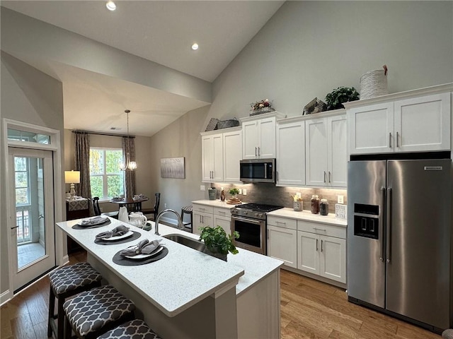 kitchen with premium appliances, a breakfast bar area, a kitchen island with sink, wood finished floors, and white cabinetry