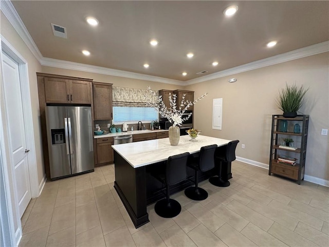 kitchen featuring stainless steel appliances, a sink, a kitchen island, visible vents, and ornamental molding