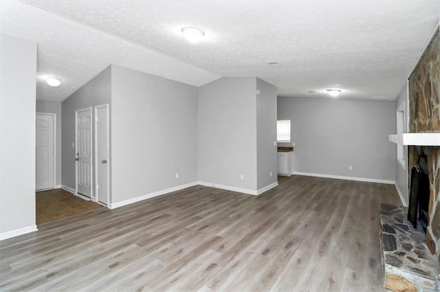 unfurnished living room with a large fireplace, vaulted ceiling, hardwood / wood-style floors, and a textured ceiling