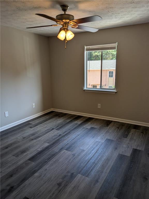 empty room with a textured ceiling, dark wood-type flooring, and ceiling fan