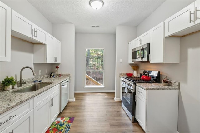 kitchen with light wood-type flooring, stainless steel appliances, white cabinetry, and sink