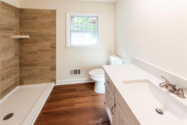 bathroom featuring wood-type flooring, a tile shower, vanity, and toilet