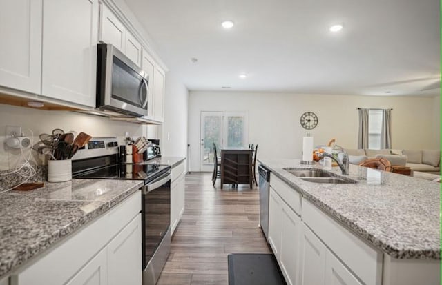 kitchen with appliances with stainless steel finishes, light stone countertops, sink, white cabinets, and light hardwood / wood-style flooring