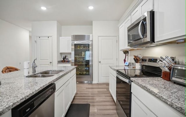 kitchen featuring white cabinetry, light wood-type flooring, stainless steel appliances, and light stone countertops