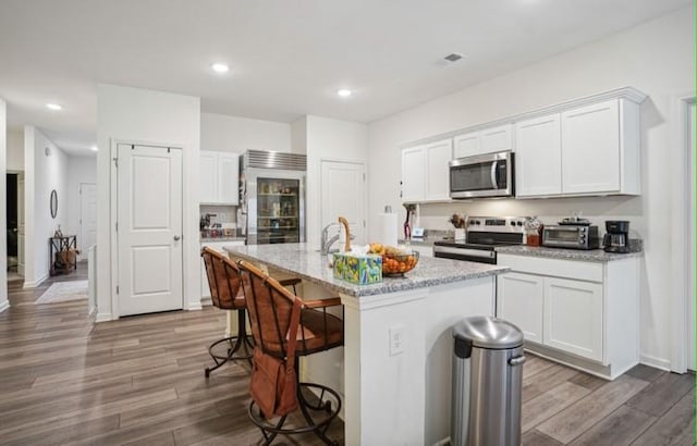 kitchen featuring a kitchen island with sink, white cabinetry, appliances with stainless steel finishes, a breakfast bar area, and light hardwood / wood-style flooring