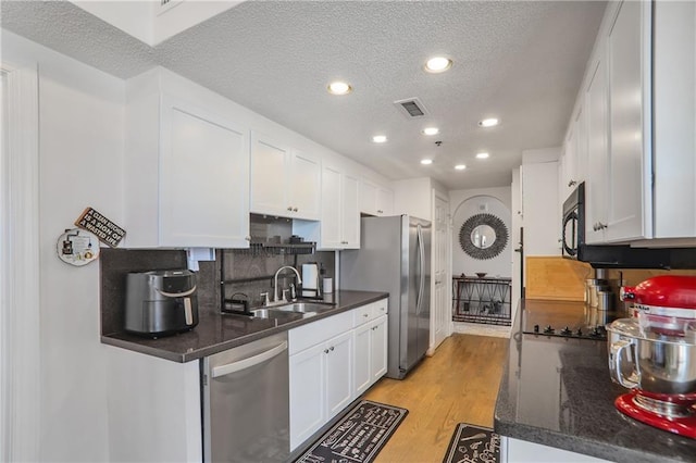 kitchen with a textured ceiling, light wood-style flooring, visible vents, white cabinets, and black appliances