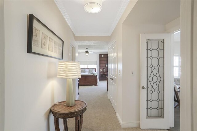 corridor with baseboards, ornamental molding, and light colored carpet