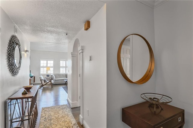 hallway with a textured ceiling, arched walkways, wood finished floors, and baseboards