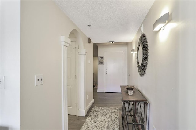 corridor with a textured ceiling, arched walkways, and wood finished floors