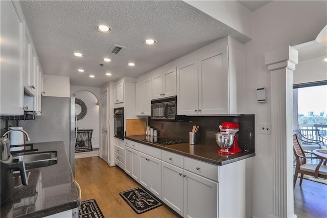 kitchen with a sink, visible vents, white cabinetry, light wood-type flooring, and black appliances