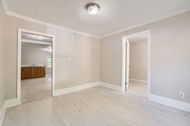 empty room with a sink, light wood finished floors, a textured ceiling, baseboards, and ornamental molding