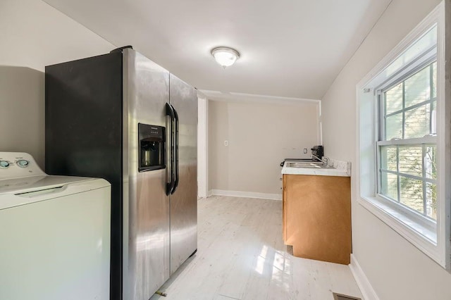 washroom featuring baseboards, a sink, washer / dryer, and light wood finished floors
