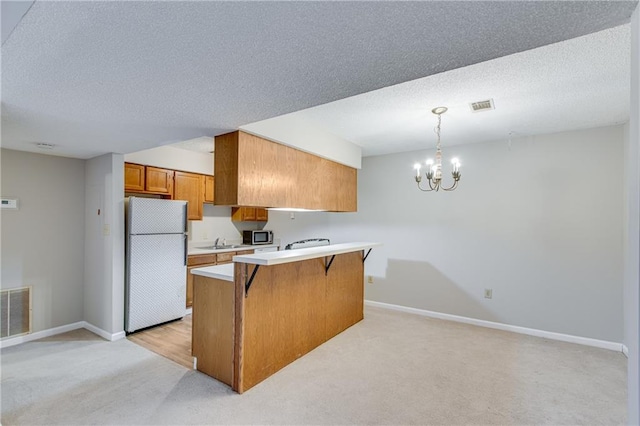 kitchen with a kitchen bar, an inviting chandelier, light carpet, hanging light fixtures, and white refrigerator