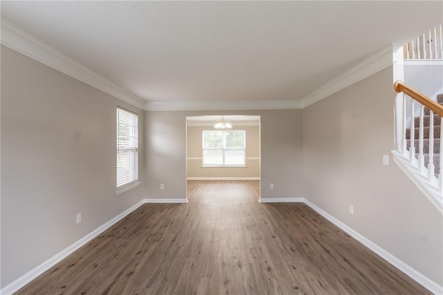 empty room featuring wood finished floors, baseboards, a chandelier, ornamental molding, and stairway