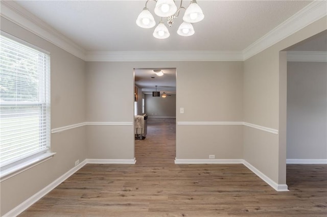 unfurnished room with plenty of natural light, a chandelier, wood finished floors, ornamental molding, and baseboards