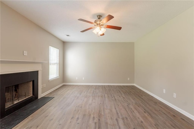 unfurnished living room featuring wood finished floors, a fireplace with raised hearth, baseboards, and ceiling fan