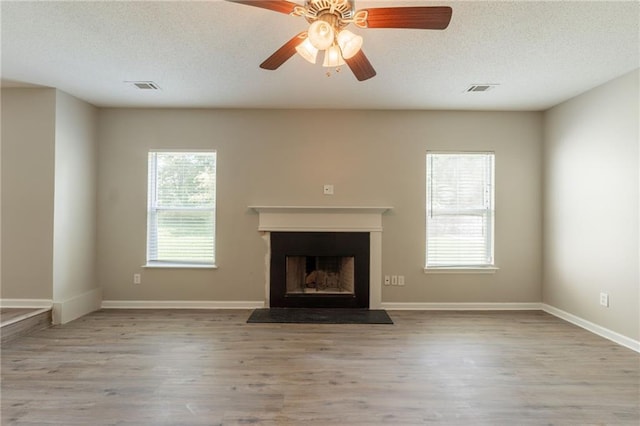 unfurnished living room with wood finished floors, a fireplace, a textured ceiling, ceiling fan, and baseboards
