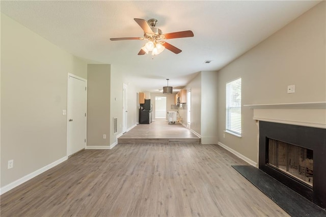 unfurnished living room featuring light wood-style floors, a fireplace with raised hearth, ceiling fan, and baseboards