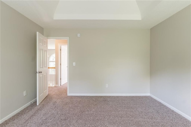 empty room with light carpet, a raised ceiling, and baseboards
